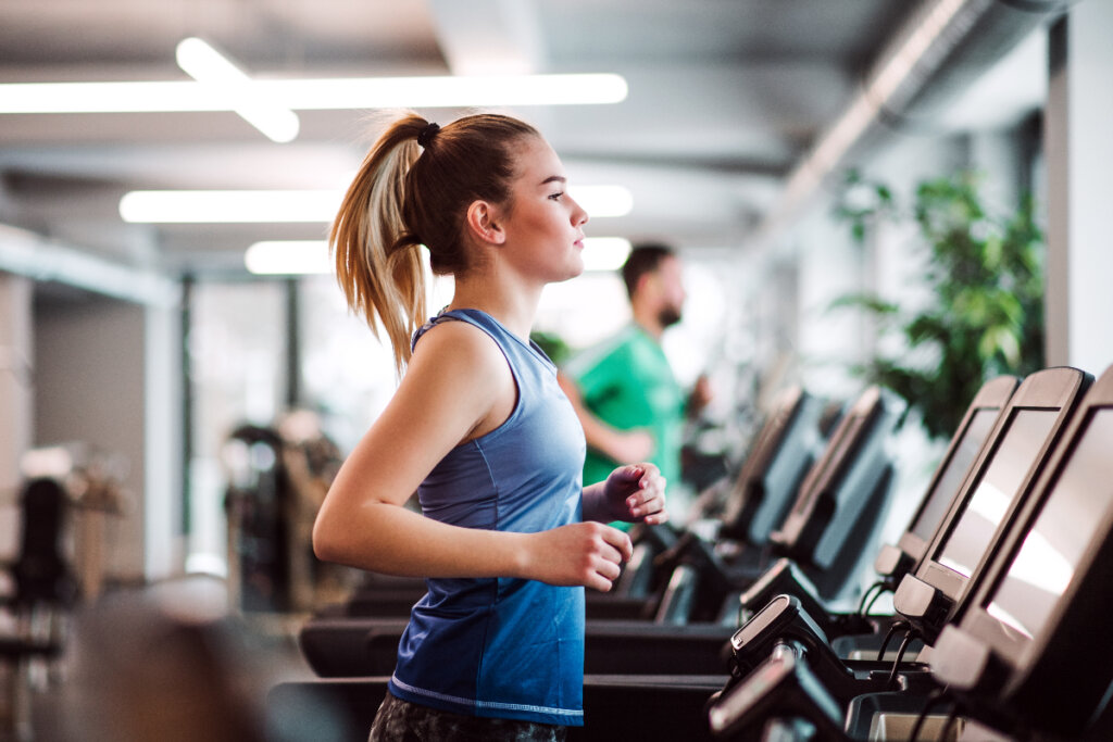 Kvinne i en blå bluse som løper på en tredemølle.  Gym scene.