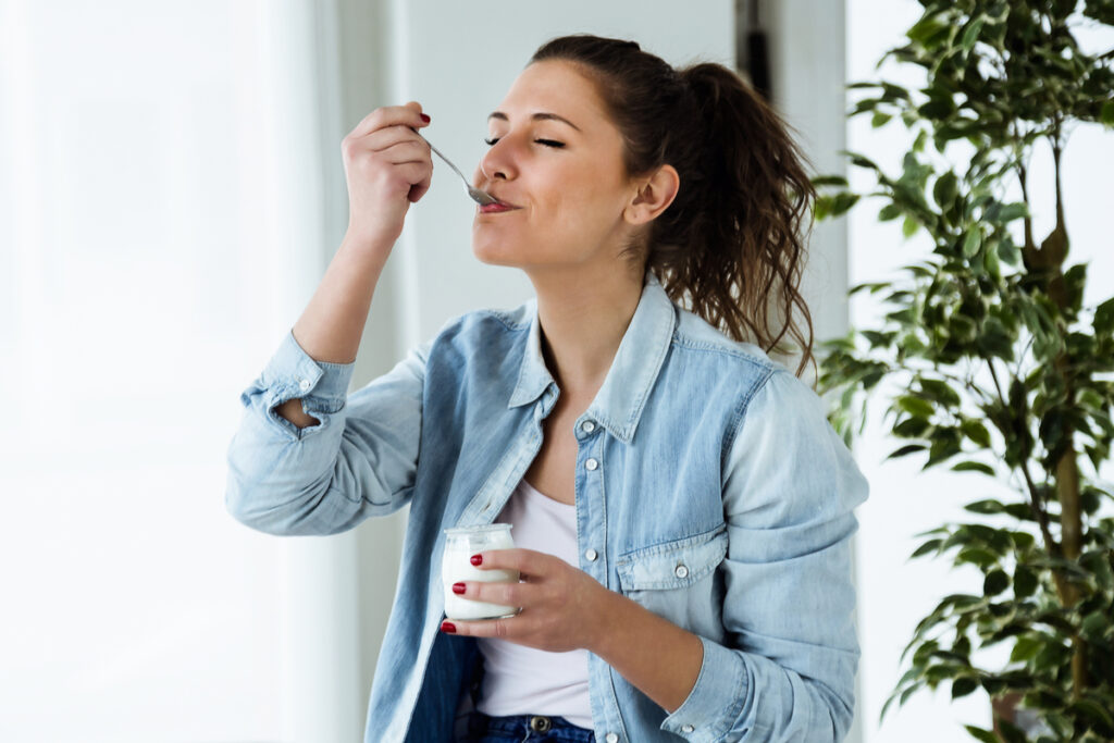 Kvinne i hvit bluse og dongerijakke spiser yoghurt