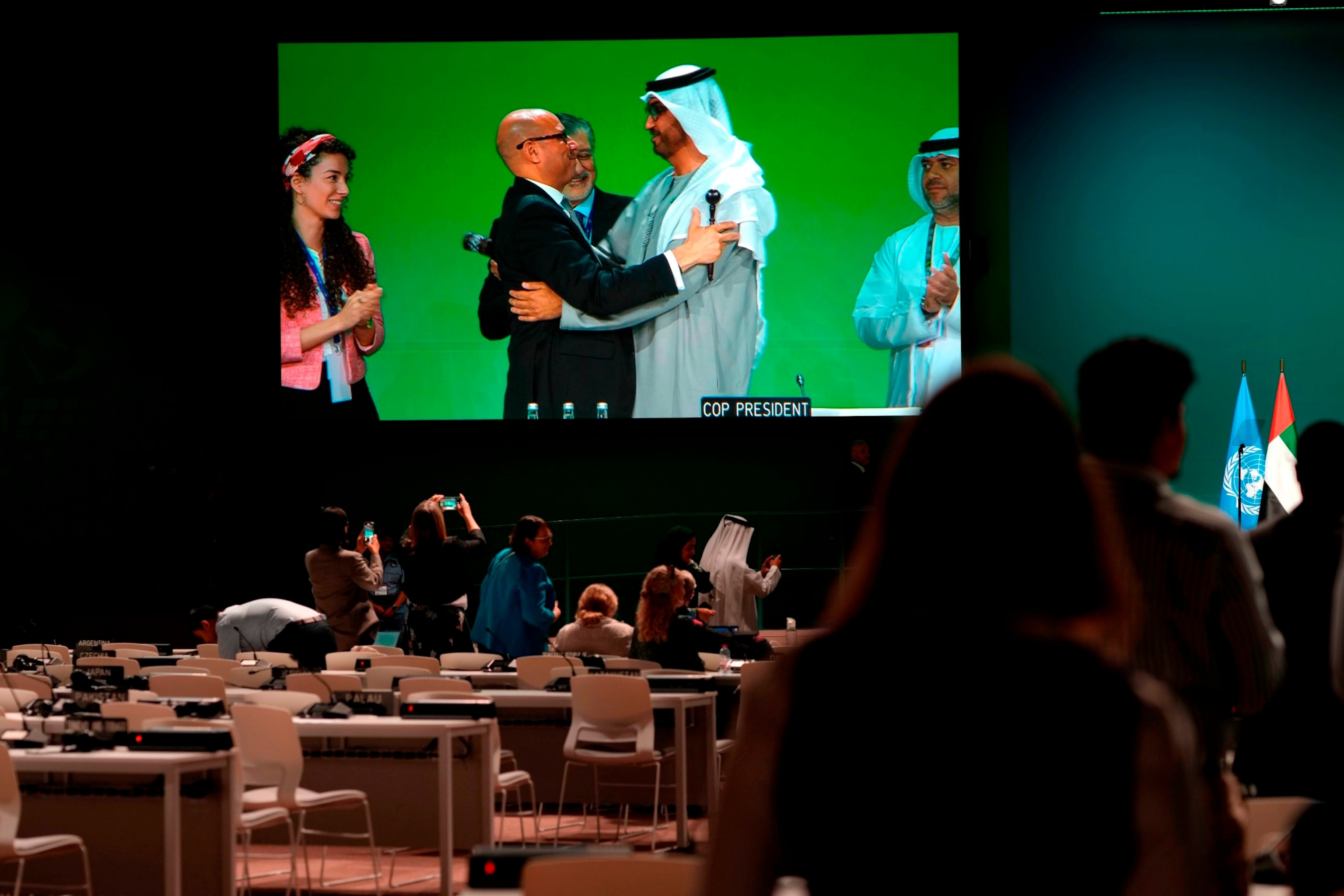 FOTO: FNs klimasjef Simon Stiell dukker opp på skjermen mens han omfavner COP28-president Sultan al-Jaber, rett, etter den siste hammeren på slutten av COP28 FNs klimatoppmøte, 13. desember 2023, i Dubai, De forente arabiske emirater.